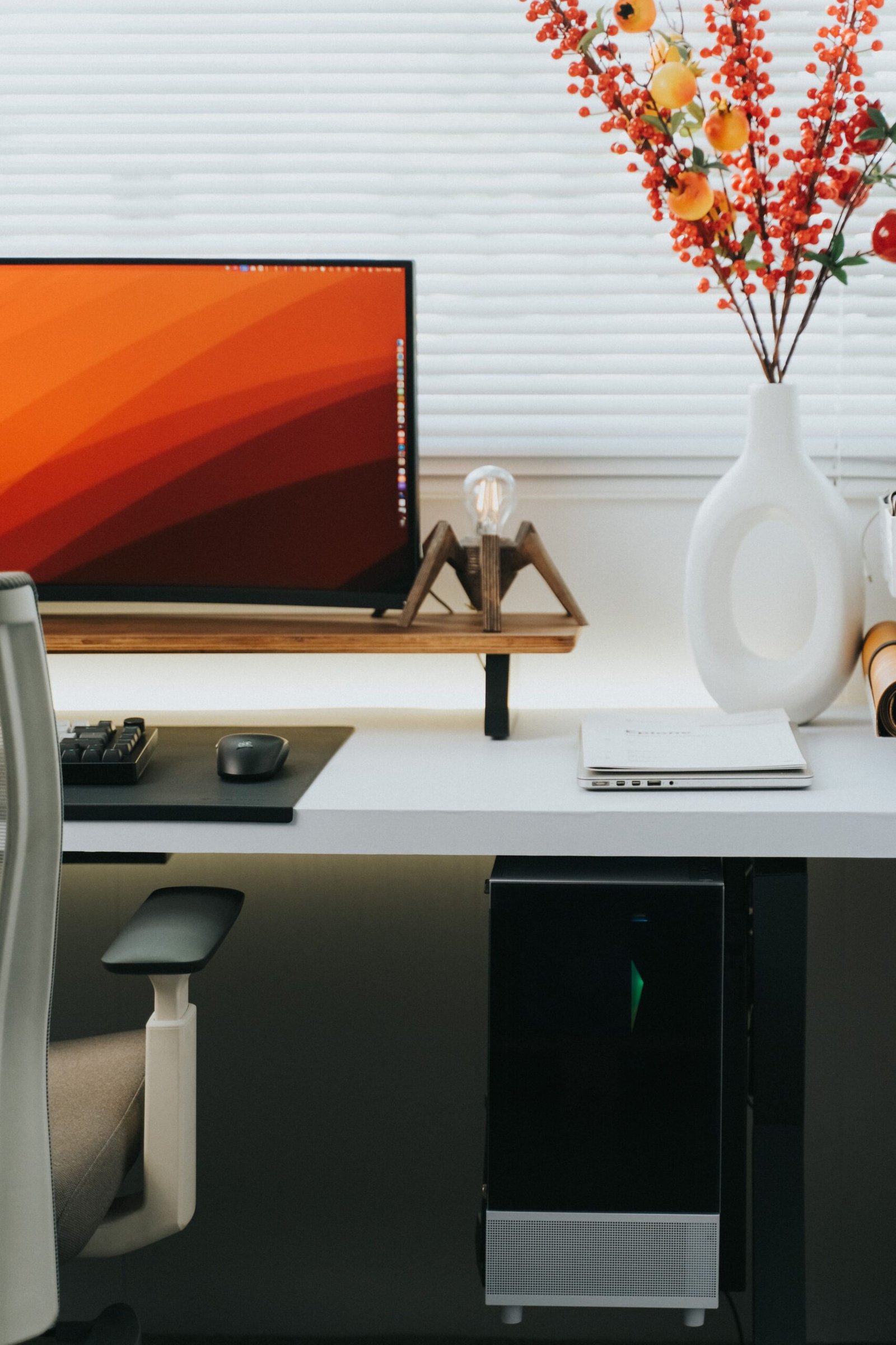 Stylish home office setting featuring a computer, ergonomic chair and decorative vase with flowers. Ideal for lumbar support improvements experts.